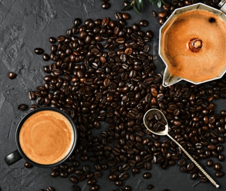 Espresso coffee with fragrant foam in a cup and in a pot and coffee beans on a black table, flat lay. Breakfast with italian cafe, coffee pot top view on table